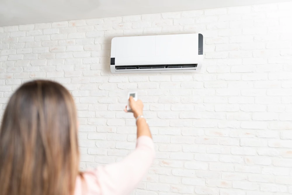 Rear view of young woman adjusting temperature of air conditioner